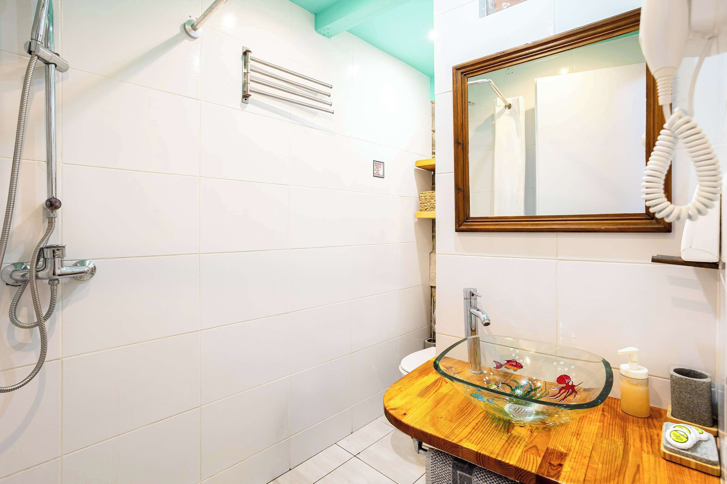 A bathroom with a glass sink, a shower, and a mirror with a towel rack.