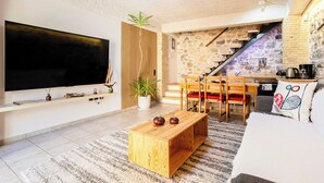 Una sala de estar con televisor, mesa de centro de madera, sofá y una escalera que da a una cocina.