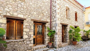 Un edificio de piedra con contraventanas de madera, plantas en macetas y una calle adoquinada.