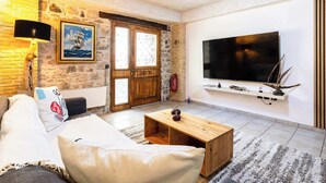 Una sala de estar con sofá, mesa de centro, pared de piedra, puerta de madera y televisor montado.