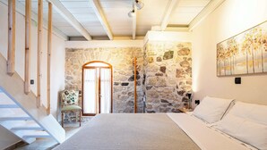 Un dormitorio con pared de piedra, cama, silla y escalera.
