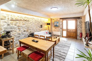 A stone-walled room with a wooden dining table, chairs, a sofa, and a fireplace.