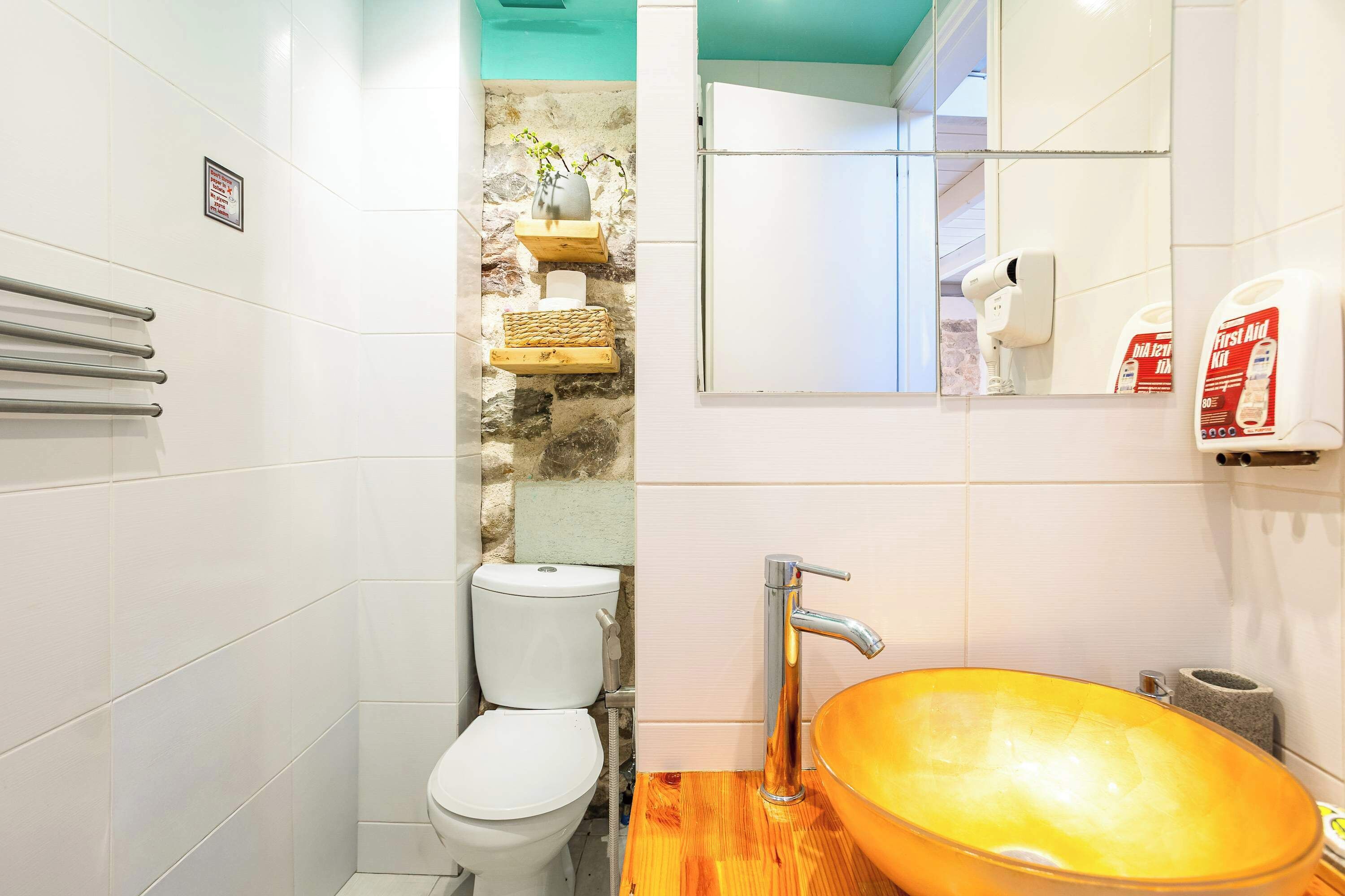 Une salle de bain avec des toilettes blanches, un meuble-lavabo en bois avec un vasque en verre, un sèche-mains et un distributeur de savon.