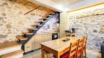 Une cuisine avec un mur en pierre, un escalier en bois et un coin repas comprenant une table et des chaises.