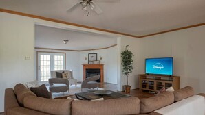 A living room with a large brown sofa, a coffee table, a fireplace, a television, and a ceiling fan.