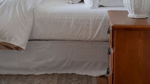 A bedroom with a bed, pillows, a nightstand, a lamp, and a wooden floor.