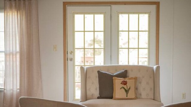 A living room with a sofa and two armchairs, a large window with curtains, and a rug on the floor.
