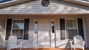 A house with a front porch, two white Adirondack chairs, and a central white door with a small window.