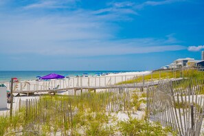 A beach with a wooden boardwalk, beach umbrellas, and a clear blue sky.