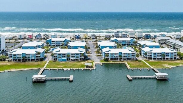 A coastal hotel with multiple blue buildings, a marina with docks, and a view of the ocean. - Sea Oats 105h 3 Bedroom Condo (Gulf Shores)