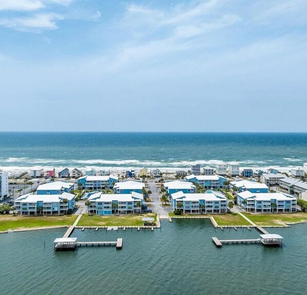 A coastal hotel with multiple blue buildings, a marina with docks, and a view of the ocean. - Sea Oats 105h 3 Bedroom Condo (Gulf Shores)