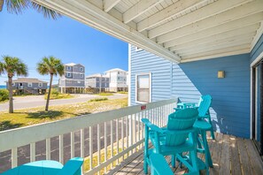 A covered porch with turquoise chairs, overlooking a beach with buildings in the background. - Sea Oats 105h 3 Bedroom Condo (Gulf Shores)