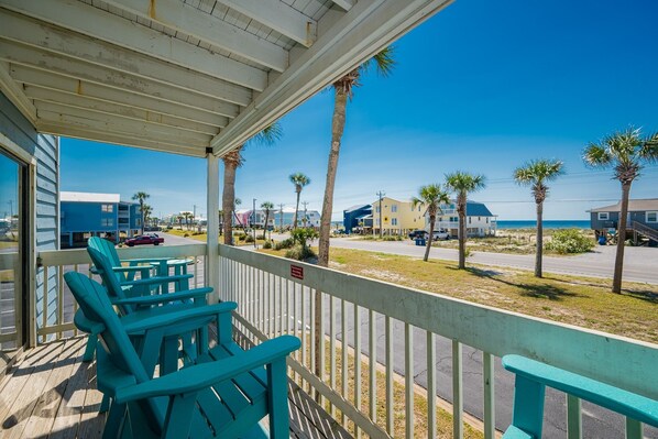 A covered outdoor area with teal chairs and a white railing, overlooking a street with palm trees and buildings. - Sea Oats 105h 3 Bedroom Condo (Gulf Shores)
