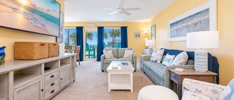 A spacious living area with a view of the beach, a ceiling fan, and a comfortable seating arrangement.