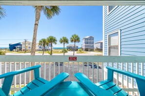 A view from a porch with a railing, overlooking a beach with palm trees and a clear sky.