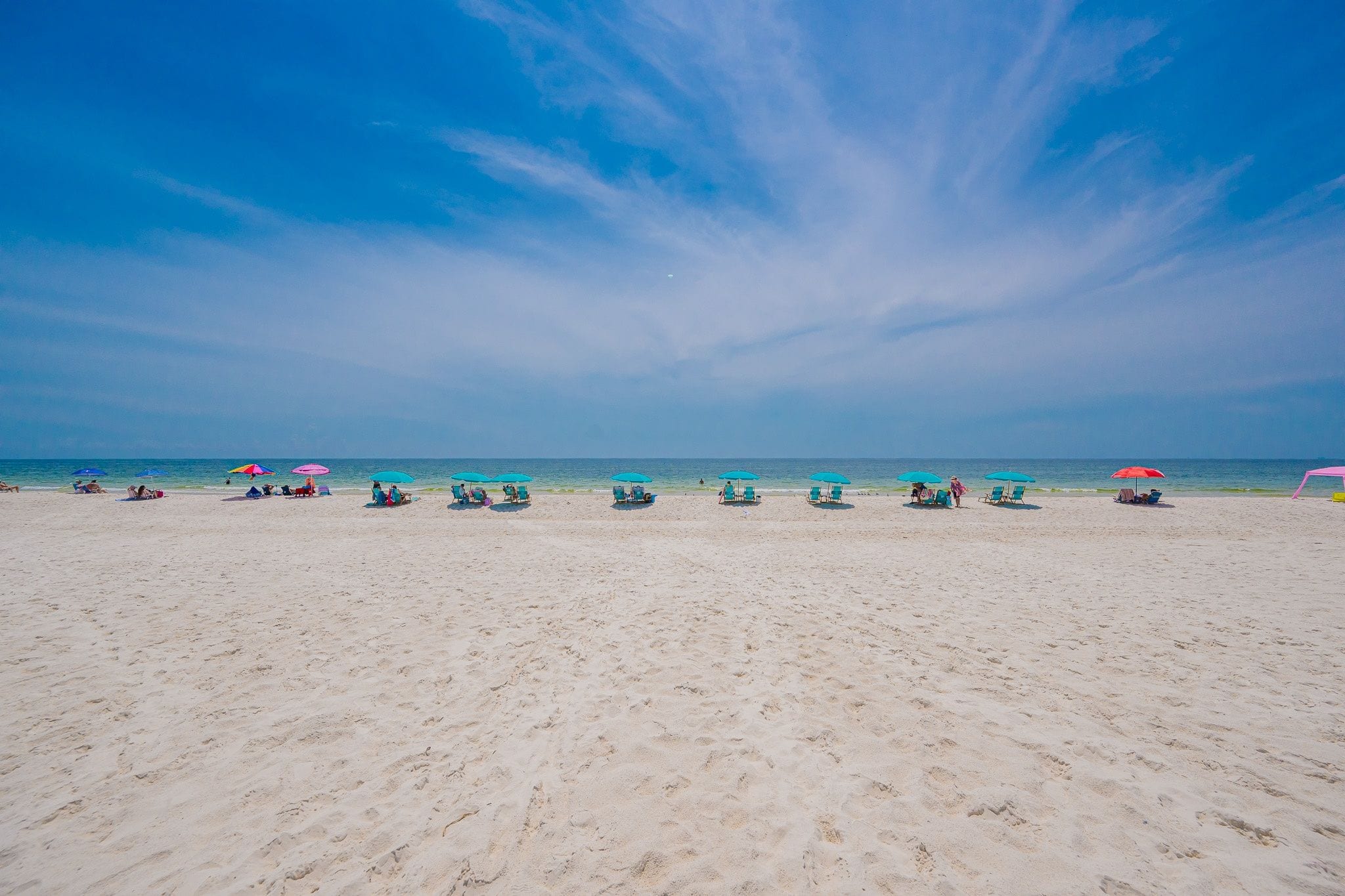 A beach with rows of sun loungers and umbrellas, a clear sky, and the ocean in the background.