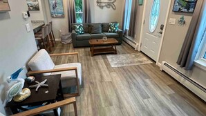 Een gezellige woonkamer met een houten plafond, een bank, een bijzettafeltje en een eethoek met stoelen.