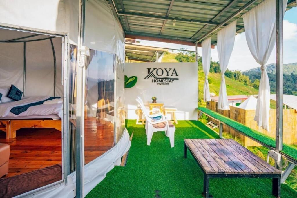 Una stanza accogliente con un letto, un tavolino e una panca. Sul muro è presente un cartello con la scritta 'KOYA HOMESTAY'.