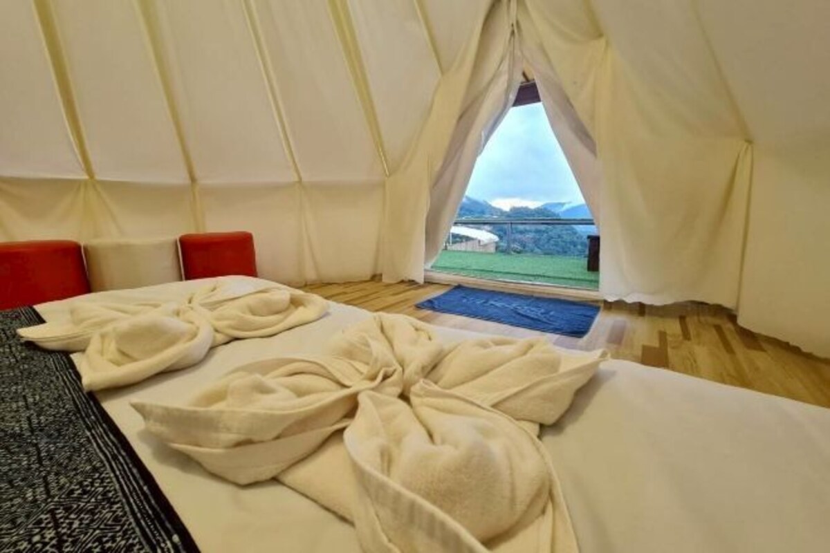 A tent-style room with a bed, two red chairs, and a view of a green landscape.