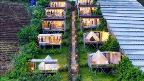A series of tents and cabins arranged in a terraced layout on a hillside, with a central pathway connecting them. - Koya Homestay (Mae Rim)
