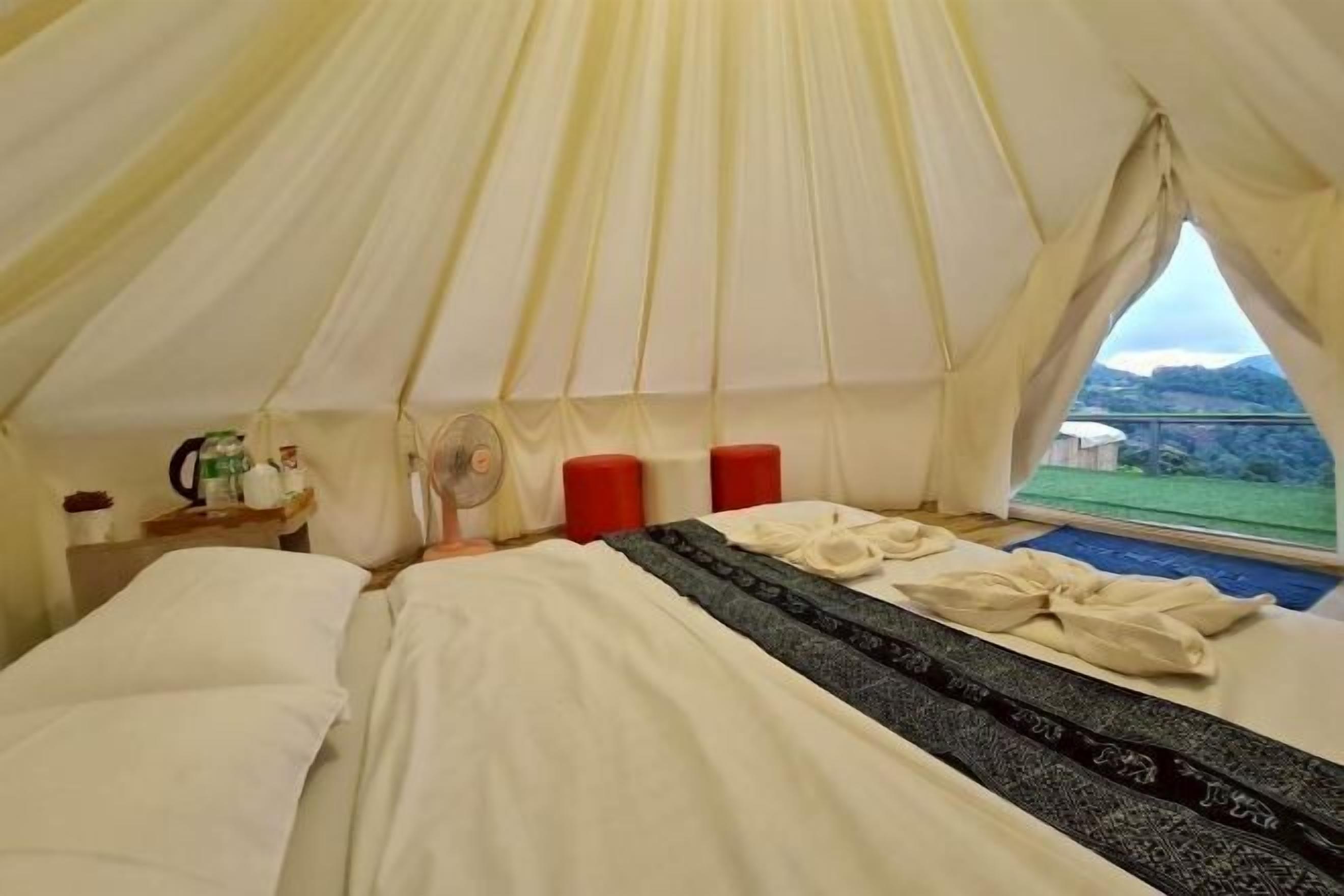Een tentkamer met een bed, een ventilator en een raam met uitzicht.