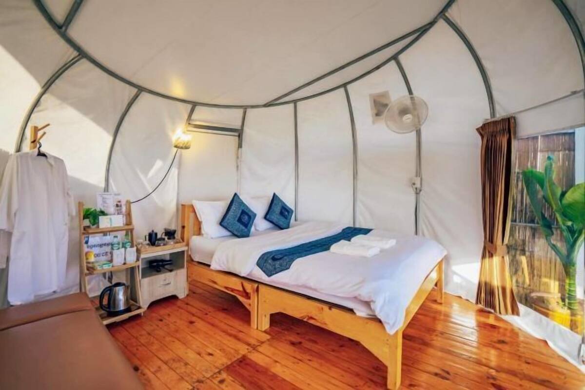 A tent-style room with a bed, bedside table, and a shelf with items.