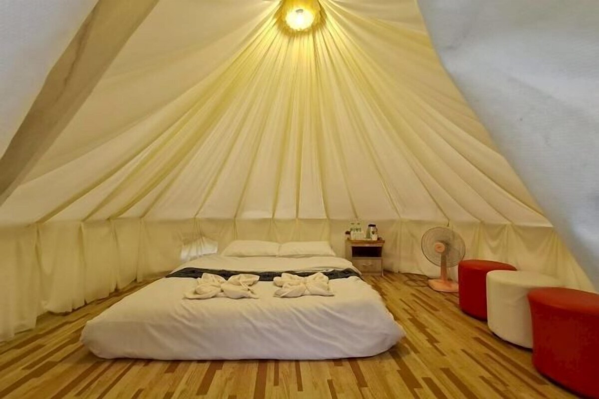 A tent-style room with a bed, bedside table, and a fan.