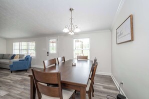 Uma sala de jantar ampla com mesa e cadeiras de madeira, um candelabro e uma citação inspiradora emoldurada na parede.