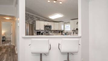 A modern kitchen with white cabinets, stainless steel appliances, and a bar area with two white stools.