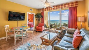 A living room with a sofa, chairs, a coffee table, and a TV. There is a balcony with a view of the ocean. - Shores Of Panama 618 2 Bedroom Condo (Panama City Beach)