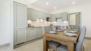 Una cocina moderna con armarios verde claro, una mesa de comedor de madera dispuesta para cuatro comensales y un microondas sobre el fregadero.