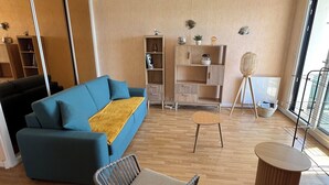 Een moderne woonkamer met een blauwe bank, een houten salontafel en een rieten stoel.