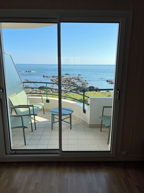 A room with a sliding glass door leading to a balcony with a view of the sea and rocks.