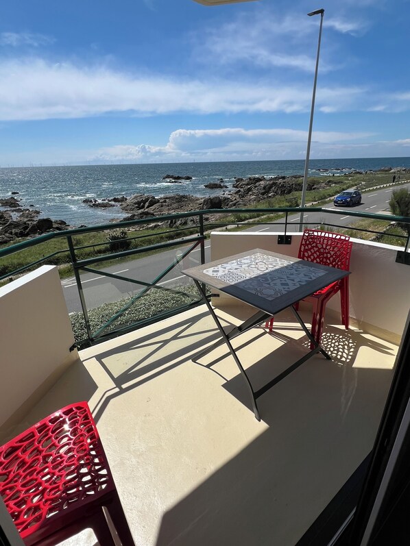 A balcony with a table and chairs, overlooking a rocky coastline and the sea.