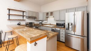 Una cocina moderna con armarios grises, electrodomésticos de acero inoxidable y una isla de madera con taburetes.