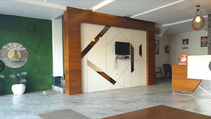 Een moderne receptie met een houten receptiebalie, een flatscreen televisie bevestigd aan een wand met een geometrisch patroon, en een groene wand met een decoratief metalen element.