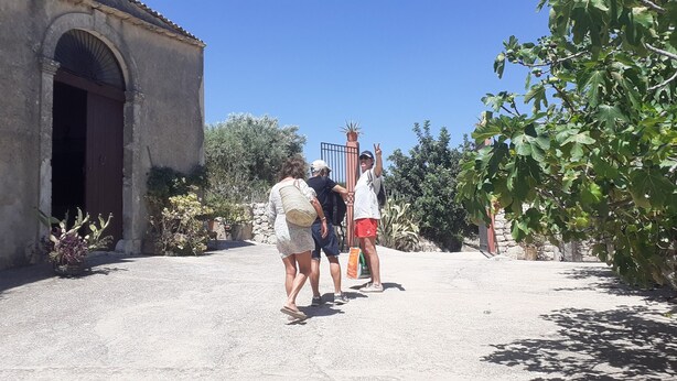 A courtyard with a stone building, a gate, and a tree. - CONTRADA CANALISI An experience on a rustic but charming farm. (NOTO)