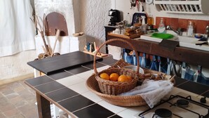 A kitchen with a tiled floor, a wooden table with a basket of oranges, a coffee machine, and various kitchen utensils. - CONTRADA CANALISI An experience on a rustic but charming farm. (NOTO)
