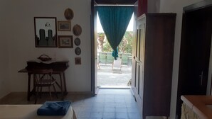 A room with a desk, chairs, and a view through a doorway to an outdoor seating area. - CONTRADA CANALISI An experience on a rustic but charming farm. (NOTO)