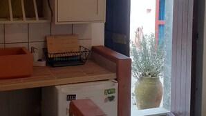 A kitchen with a stone countertop, a wooden table, and a potted plant visible through an open door. - CONTRADA CANALISI An experience on a rustic but charming farm. (NOTO)