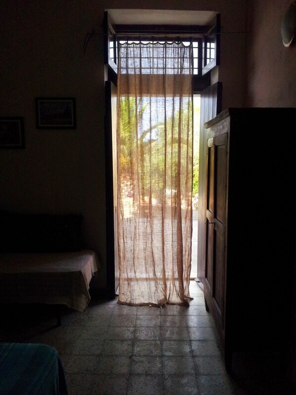 A room with a bed, a wooden cabinet, and a window with a sheer curtain.