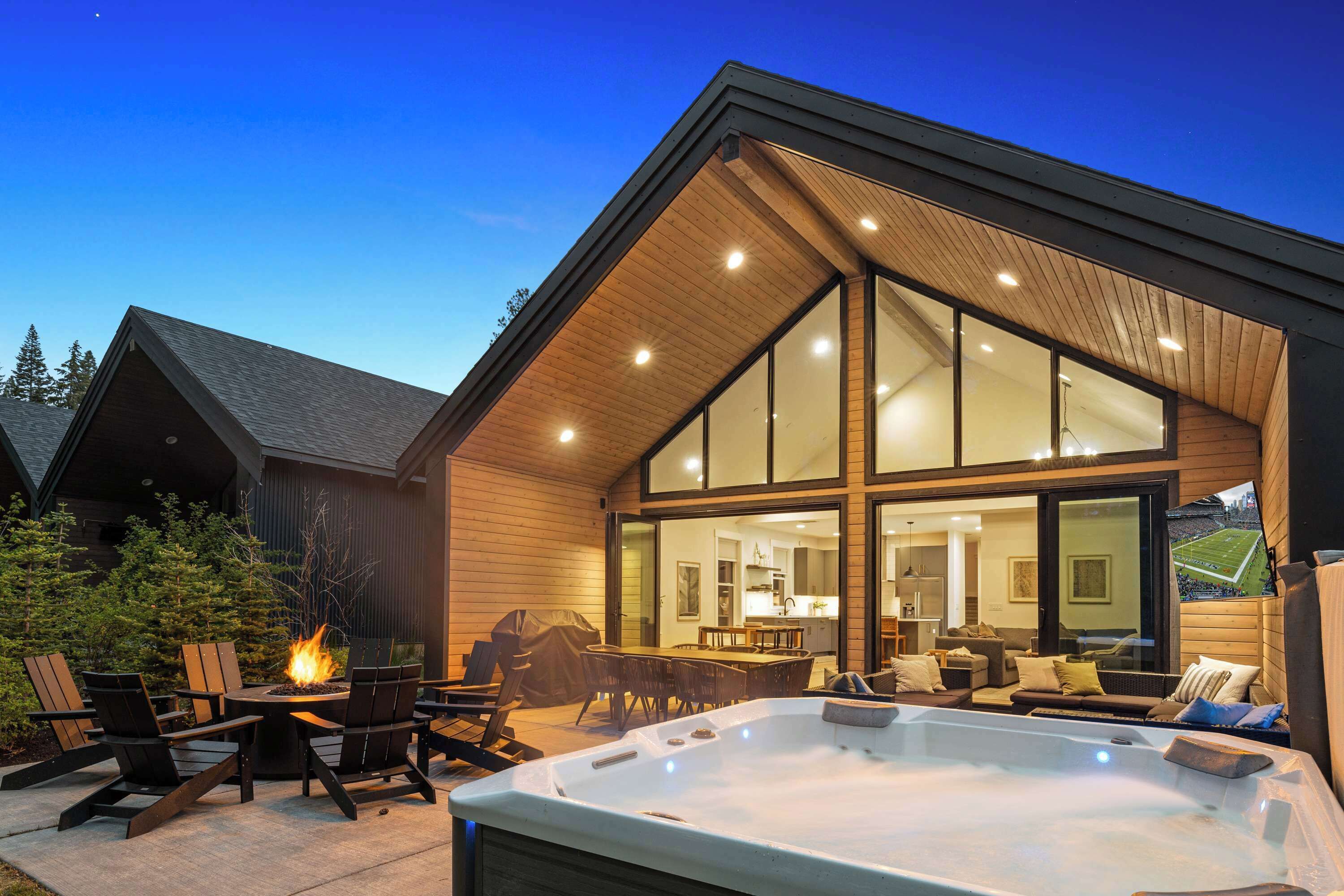 A modern house with a large glass window, a hot tub, and outdoor seating.