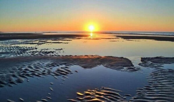 Ein Strandbild mit untergehendem Sonnenuntergang über dem Wasser, das eine ruhige und spiegelnde Oberfläche erzeugt.