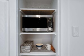 A kitchen with a microwave on the upper shelf, a patterned box, a bowl, and a rolling pin on the lower shelf.