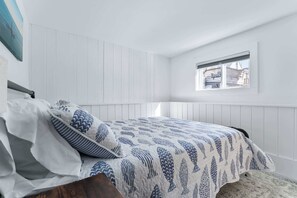 Ein Schlafzimmer mit einem Bett, weißen Wänden, einem Fenster und Blick ins Freie.