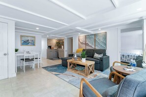 Ein modernes Wohnzimmer mit Sofa, Couchtisch und Essbereich. Im Hintergrund ist eine Küche mit Steinrückwand zu sehen.