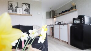 A modern kitchen with a black refrigerator, microwave, and stove. There is a dining area with a black sofa and a vase with flowers. - Cottages in Friesland With Farm Experience (Tjerkgaast)