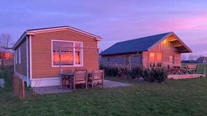 A wooden cabin with a porch and a dining area, surrounded by a grassy yard. - Cottages in Friesland With Farm Experience (Tjerkgaast)