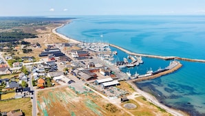An aerial view of a coastal town with a marina, residential buildings, and a sandy beach.