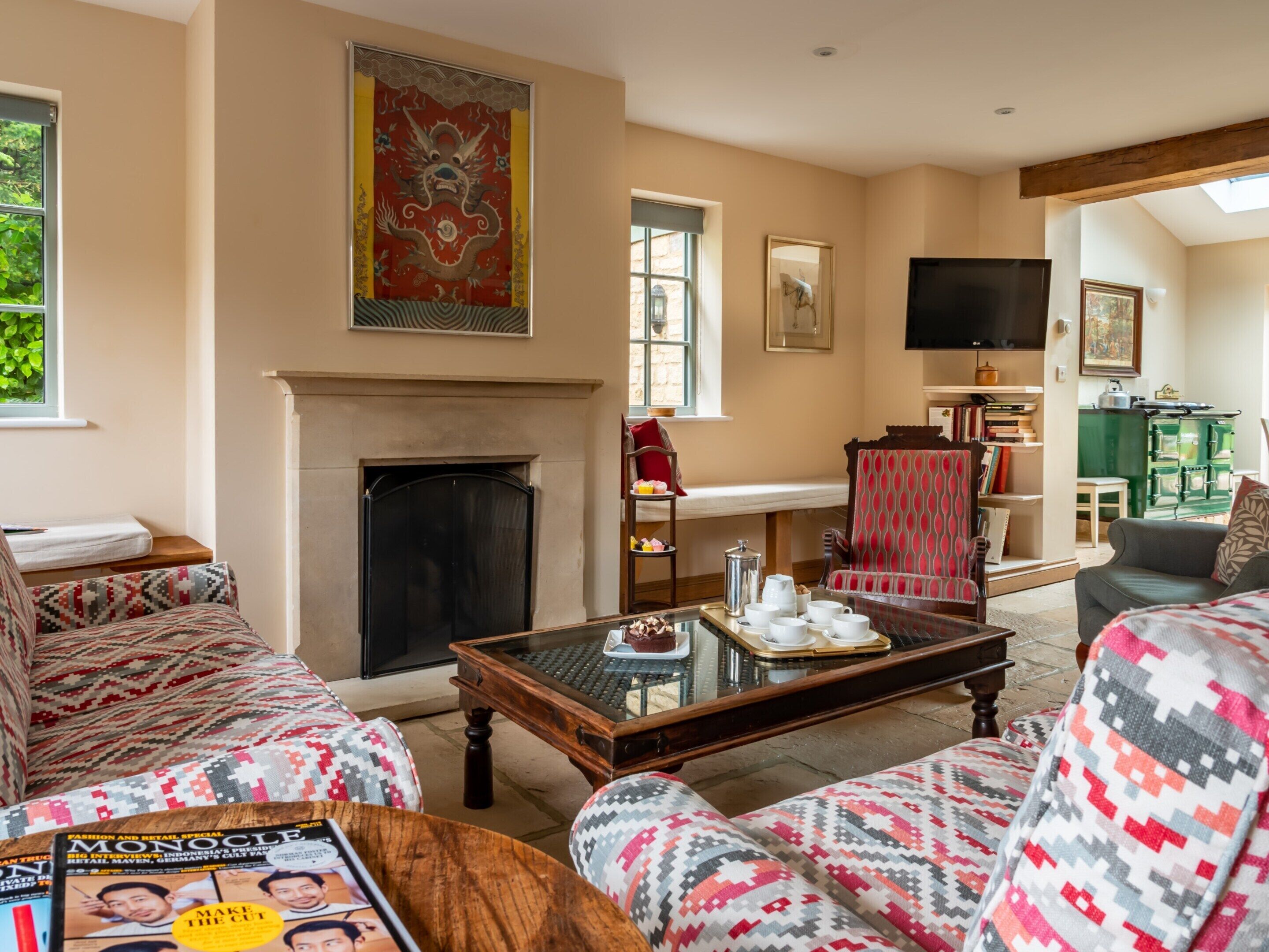 A living room with patterned furniture, a fireplace, a television, and a kitchen area in the background.